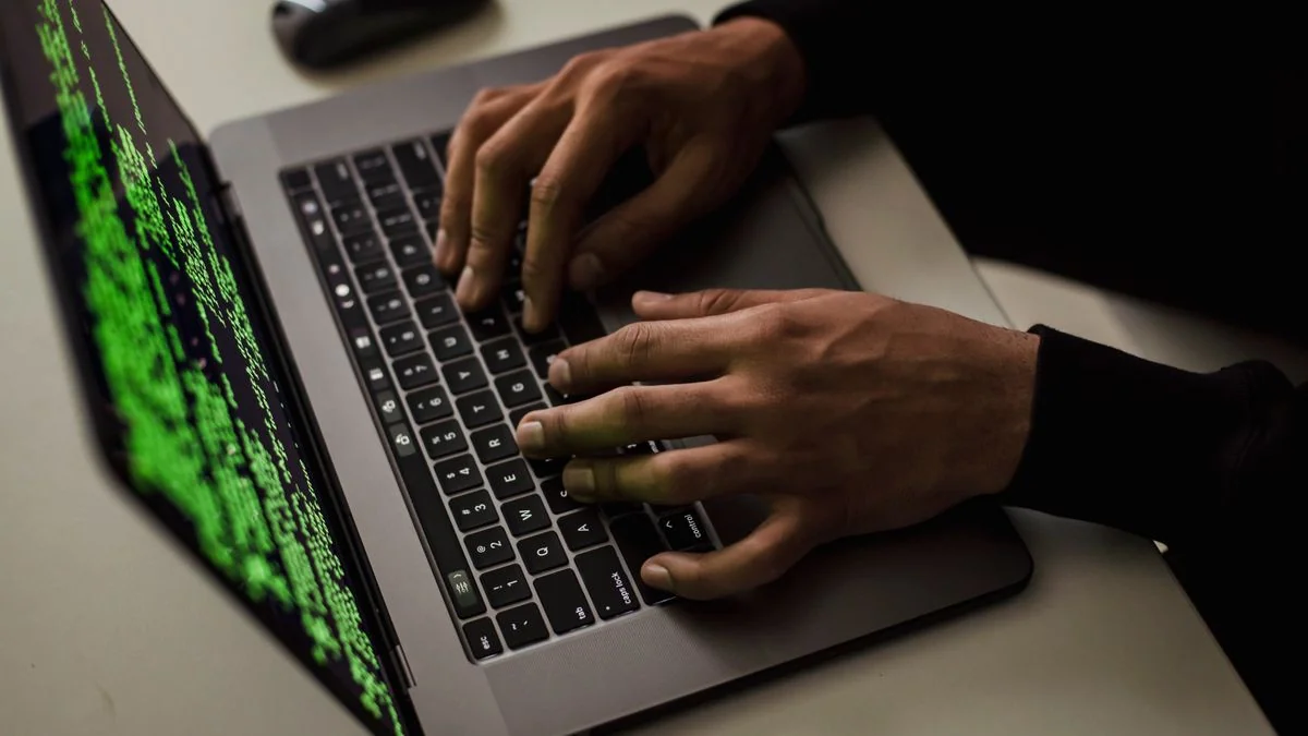 Mãos digitando em um laptop com código na tela, ilustrando ameaças e defesa em cibersegurança
